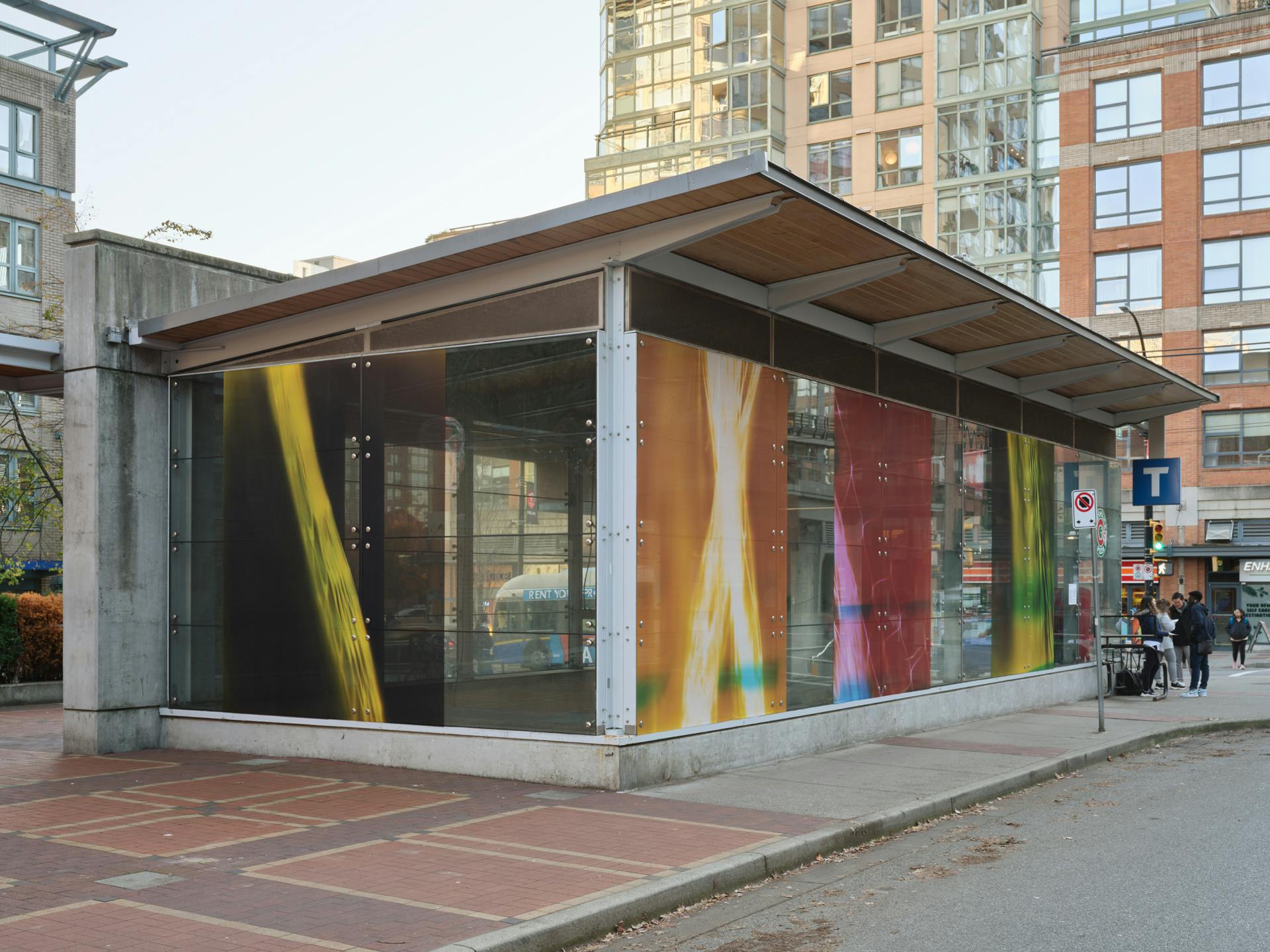 A diagonal view of a SkyTrain station with four photograms in its windows, each depicting various forms of nylon mesh bags against neon photographic paper.