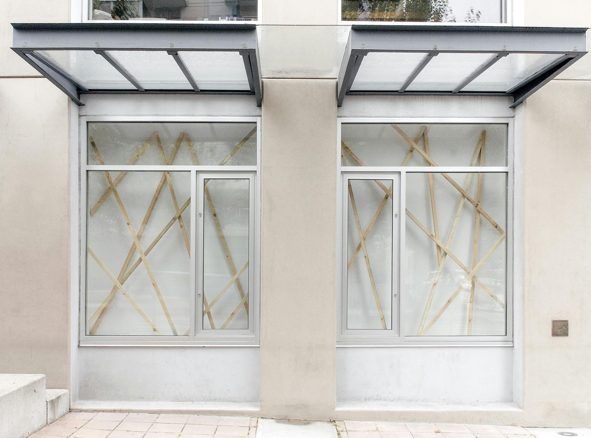 This image shows two of CAG’s window spaces, in which Elspeth Pratt’s installation art is displayed. Thin wooden bars are diagonally placed. These bars do not parallel to each other. 